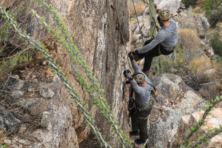 A photo of an Airman rappelling down a rock