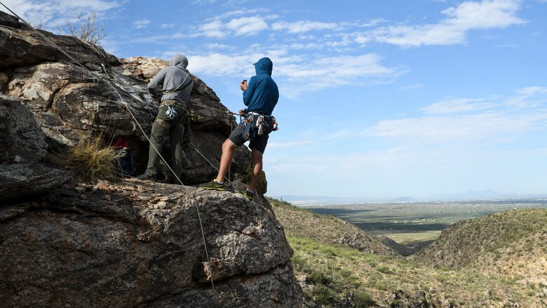 A photo of an Airman rappelling down a rock