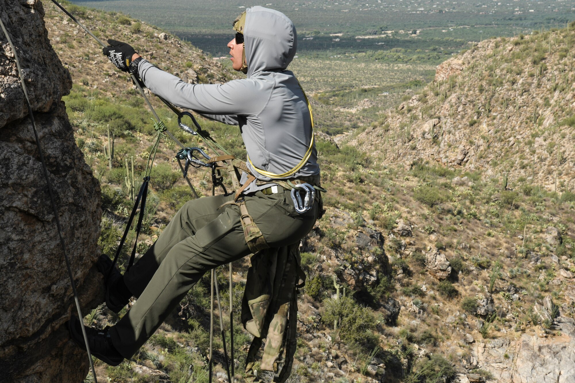 A photo of an Airman rappelling down a rock