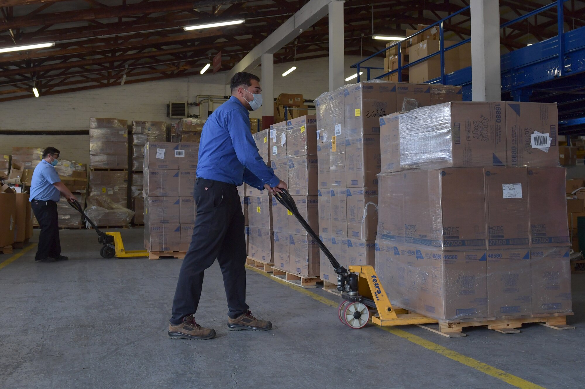 Two people moving pallets of boxes in a warehouse.