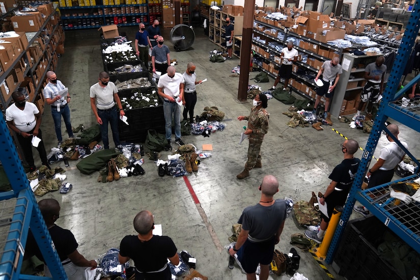 An airman hands out uniform items to trainees.
