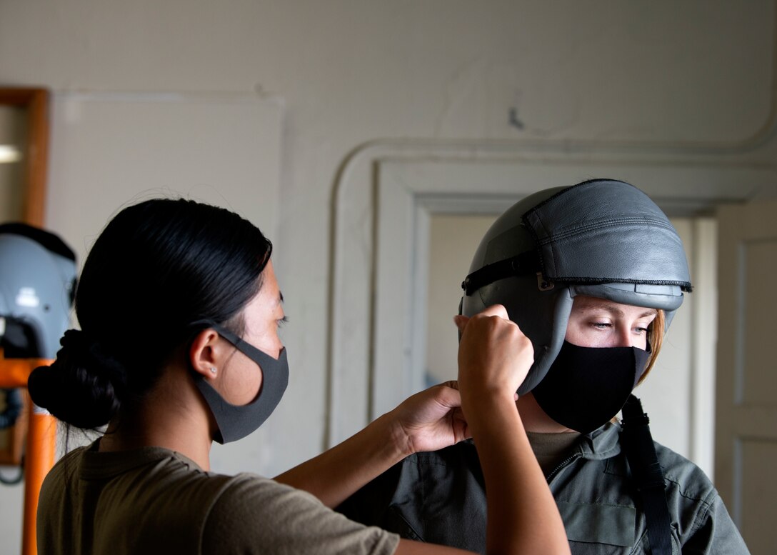 An Aircrew Flight Equipment Airman assists a pilot with her helmet during Aviation Training Relocation at Chitose Air Base, Japan Aug. 26, 2020.