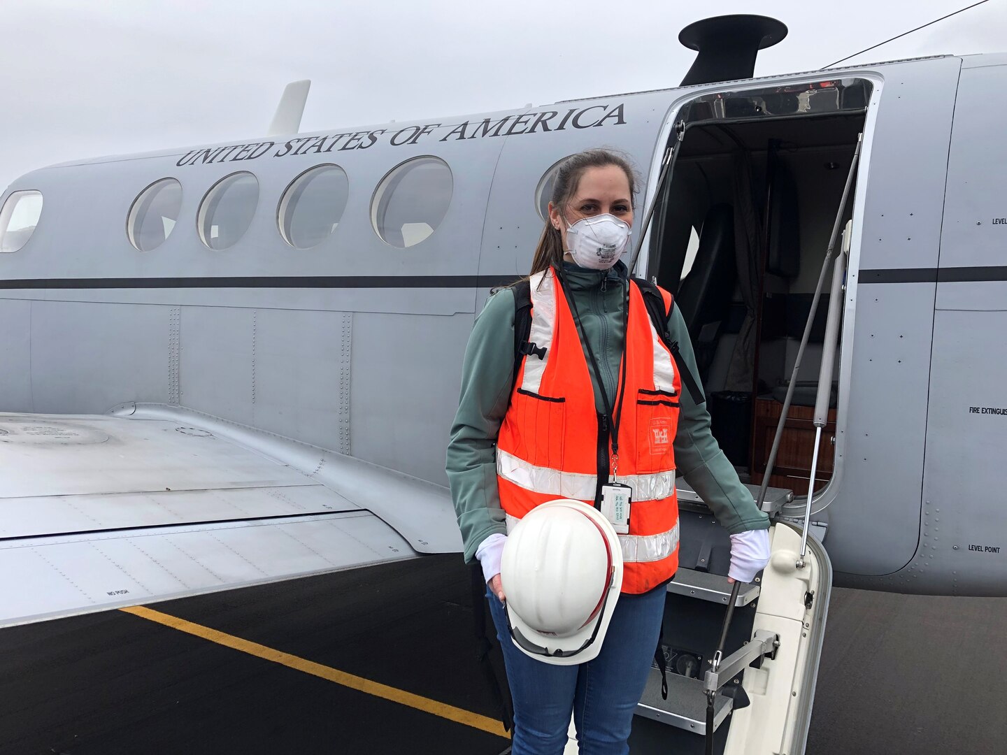 masked woman stands on stairs of airplane