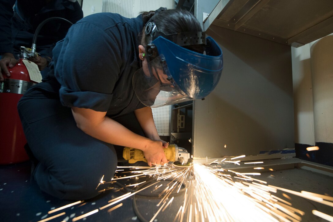 A sailor cuts a piece of equipment as sparks fly.