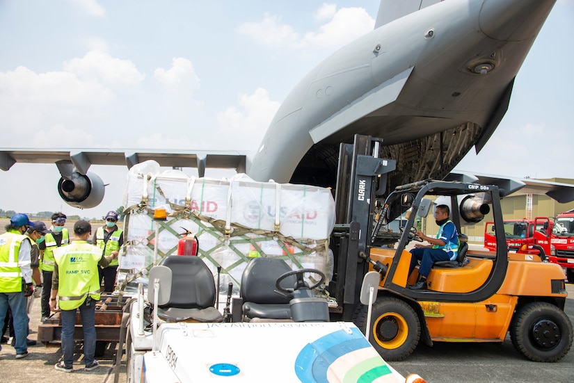 A man driving a forklift moves boxes secured to pallets from an airplane.