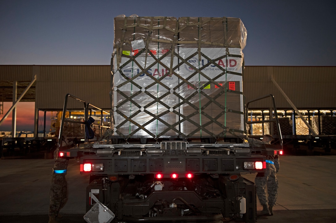 Service members secure pallets loaded with boxes to the back of a big truck.
