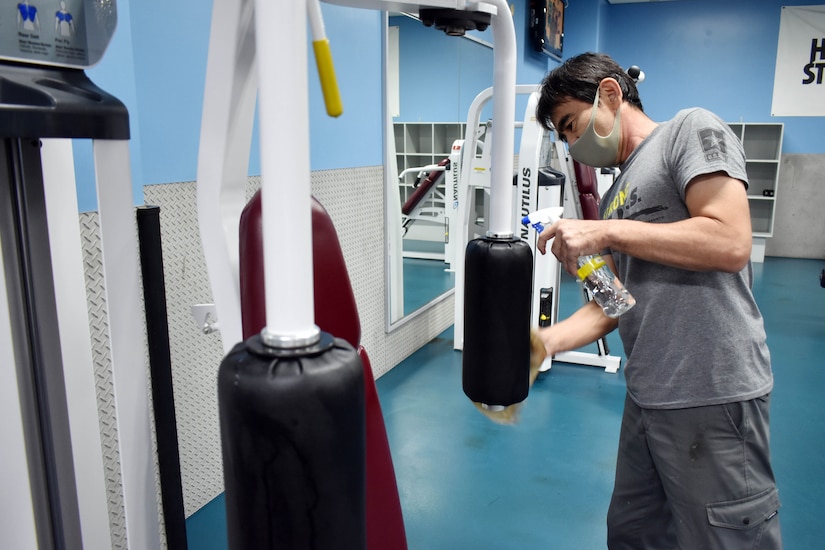 A man wearing a face mask is  cleaning exercise equipment.