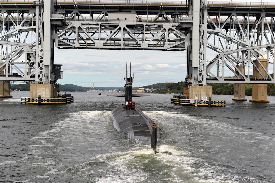A submarine moves through waters underneath a bridge.