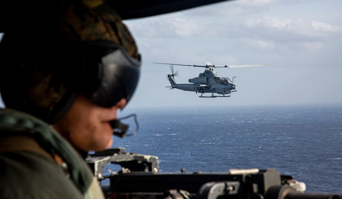 A U.S. Marine Corps UH-1Y Venom helicopter crew chief, with Marine Light Attack Helicopter Squadron 469 (HMLA-469), looks out the side door of the aircraft while flying alongside an AH-1Z Viper to a live-fire range in Okinawa, Japan, Nov. 3, 2020. HMLA-469 conducted a live-fire training event to simulate fighting in a forward operating environment to enhance the squadron’s combat readiness. (U.S. Marine Corps photo by Cpl. Ethan M. LeBlanc)