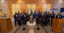 A group of Airmen in dress blues gather around an award and look to the camera for a photo.