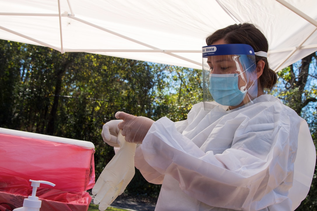 A woman wearing personal protective equipment puts on gloves.