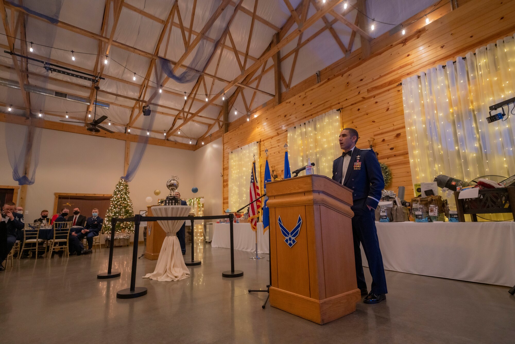 Male Airman stands at a podium next to an award and speaks to an audience.