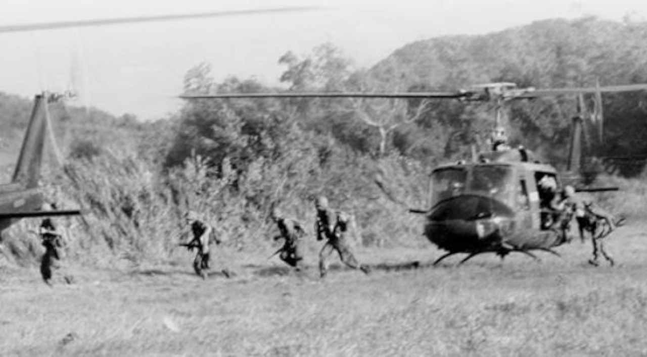 Several soldiers run from a helicopter landing in a field.