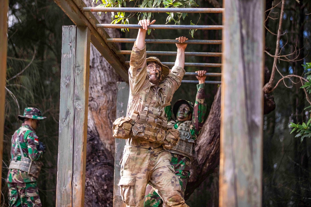 A soldier and an Indonesian service member scale monkey bars.