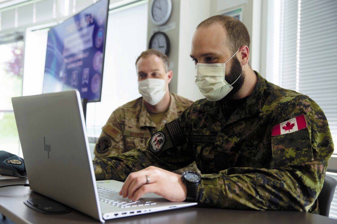 Two men in combat uniforms collaborate over a laptop.