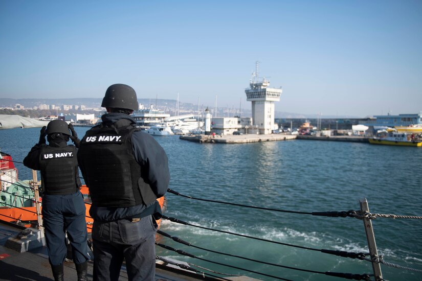 Sailors stand on the deck of a ship.