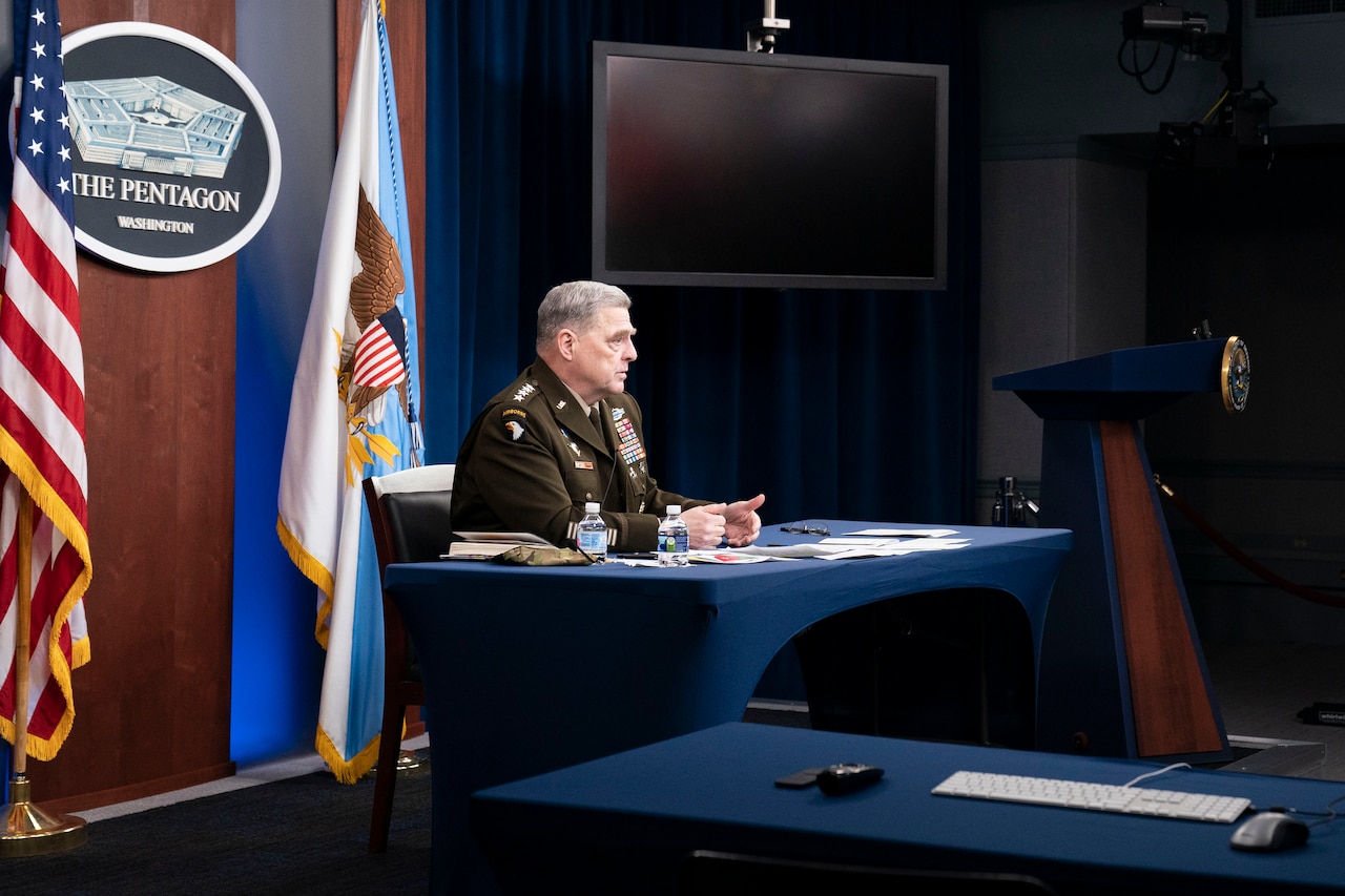 An Army general sits at a table with a Pentagon sign hanging behind him.