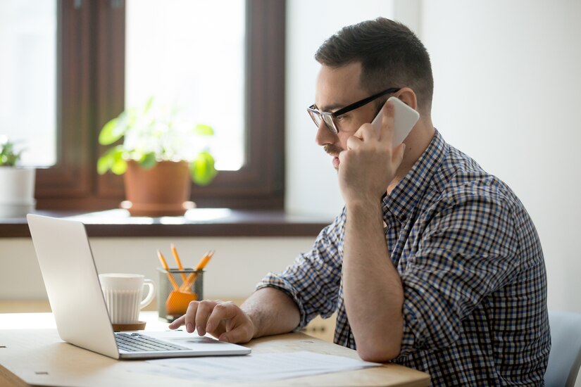 man works on the computer while on the phone