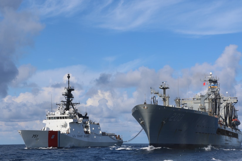 Two ships sit beside one another with a cable stretched between them. U.S. Coast Guard is written on the side of one ship.