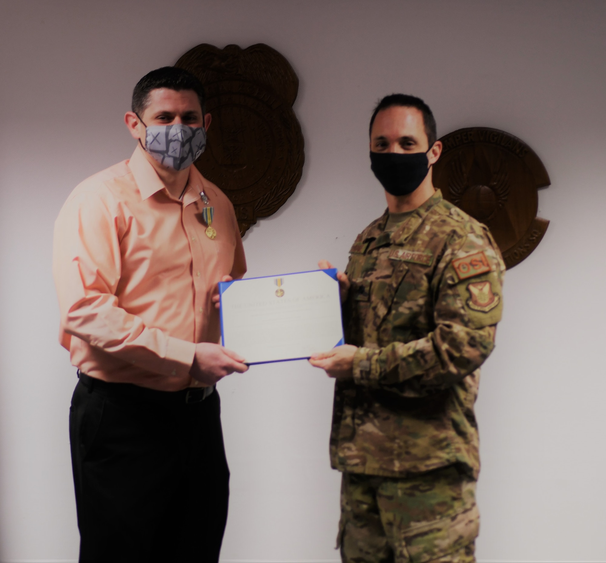 Special Agent Justin Acree accepts the Military Outstanding Volunteer Service Medal from OSI 4th Field Investigations Squadron Commander, Lt. Col. John Longmire Nov. 23, 2020. SA Acree spearheaded a volunteer effort resulting in the manufacture of 11,349 reusable masks for communities across Germany. SA Acree personally made 1,556 face coverings to help cope with the COVID-19 pandemic. (Photo by SA Phillip Santomauro, 4 FIS)