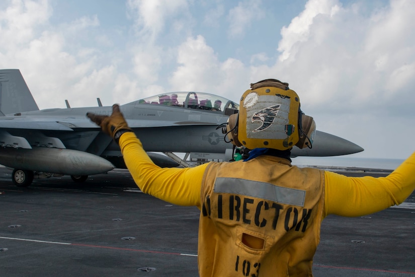 A sailor directs a jet on an aircraft carrier.