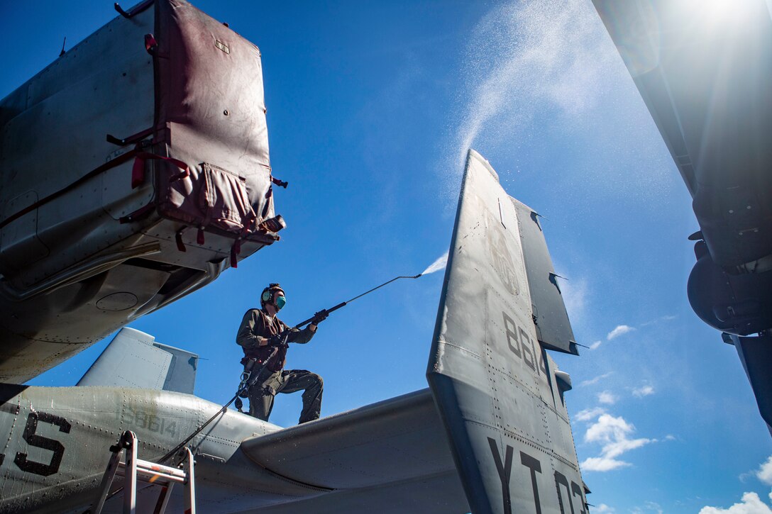 A Marine stands on an aircraft and power washes the wing.