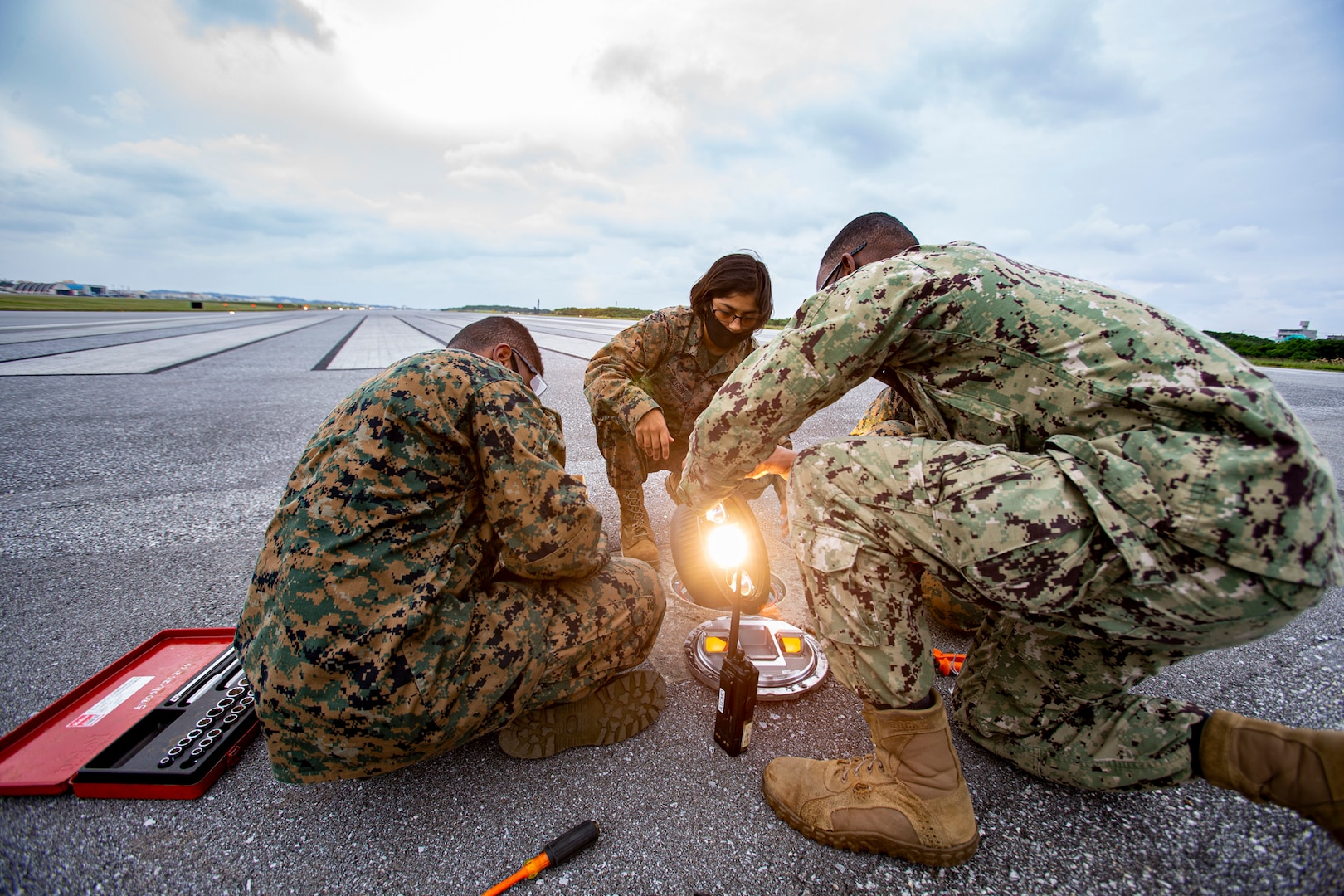 U.S. Marines with General Facilities (GF) and Navy Construction Electrician 2nd Class Ira Mozee, a native of Saint Lucie, Florida, repair threshold lights on the airfield during on-the-job training with Seabees, on Marine Corps Air Station Futenma, Okinawa, Japan, Dec. 3, 2020. When a service ticket is issued, GF Marines shadow Seabees to learn their side of the job. Seabees are trained to build and maintain permanent structures while Marines are trained in expedient construction and maintenance. The training is hands-on, teaching Marines how to build, plumb and power structures to code for long term use.