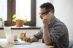 man works on the computer while on the phone