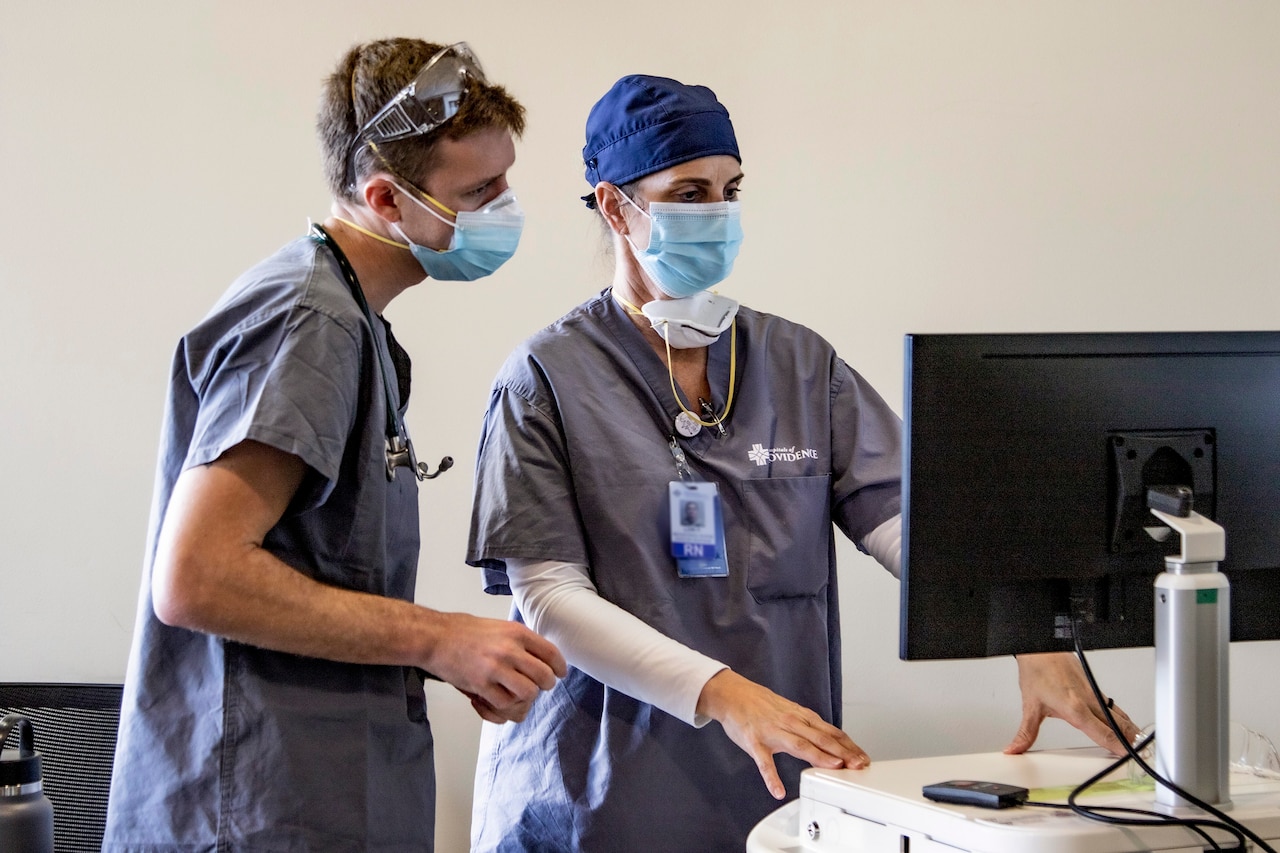 Two Air Force nurses in masks and scrubs look at a computer screen.