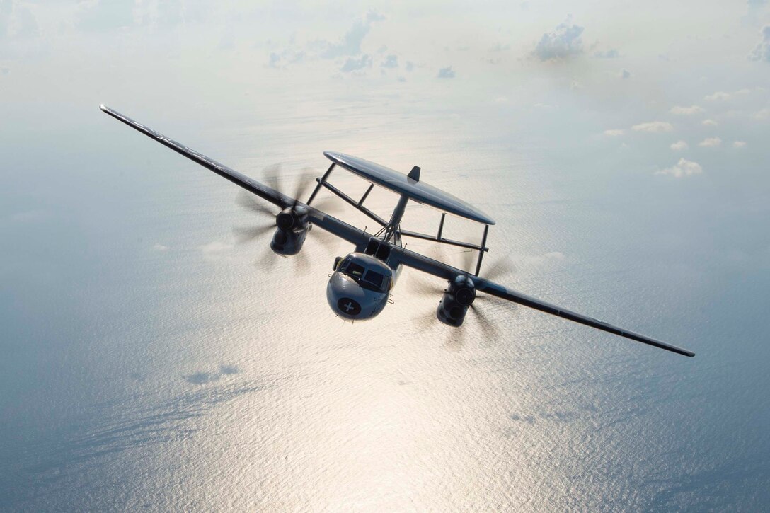 A Navy aircraft flies above water.