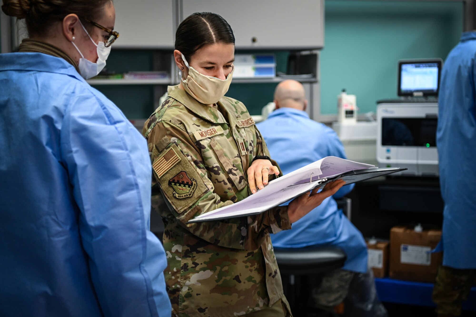 Capt. Jenifer Mouser, 66th Medical Squadron Laboratory officer in charge, center, discusses COVID-19 testing procedures with Airman 1st Class Kaylin Rice, laboratory technician, at the Hanscom Air Force Base, Mass., clinic, Dec. 3. The five-Airman team is responsible for collecting and testing all routine lab work as well as COVID tests taken on the installation. (U.S. Air Force photo by Todd Maki)