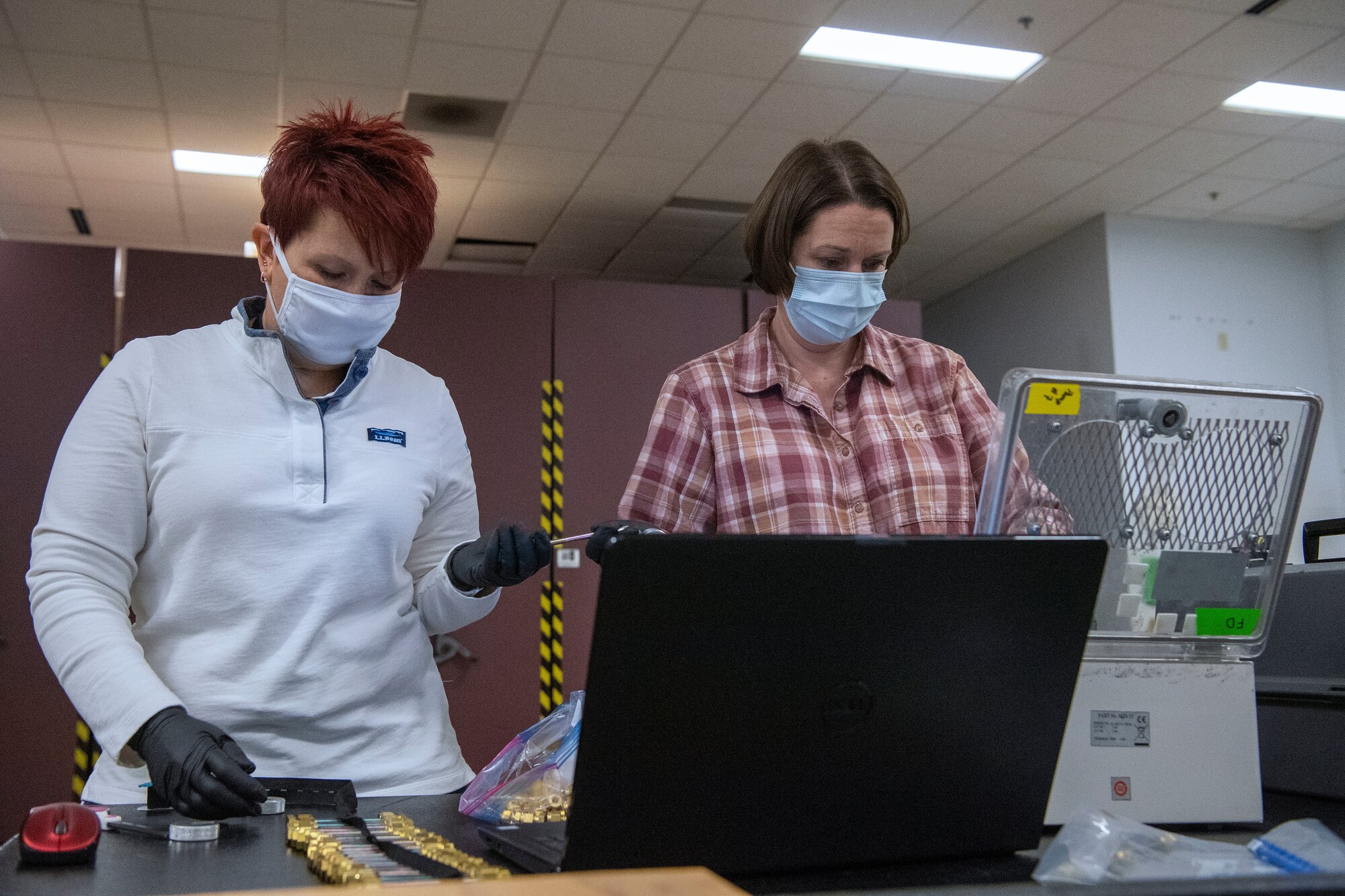 two women standing at table working while wearing mask and gloves