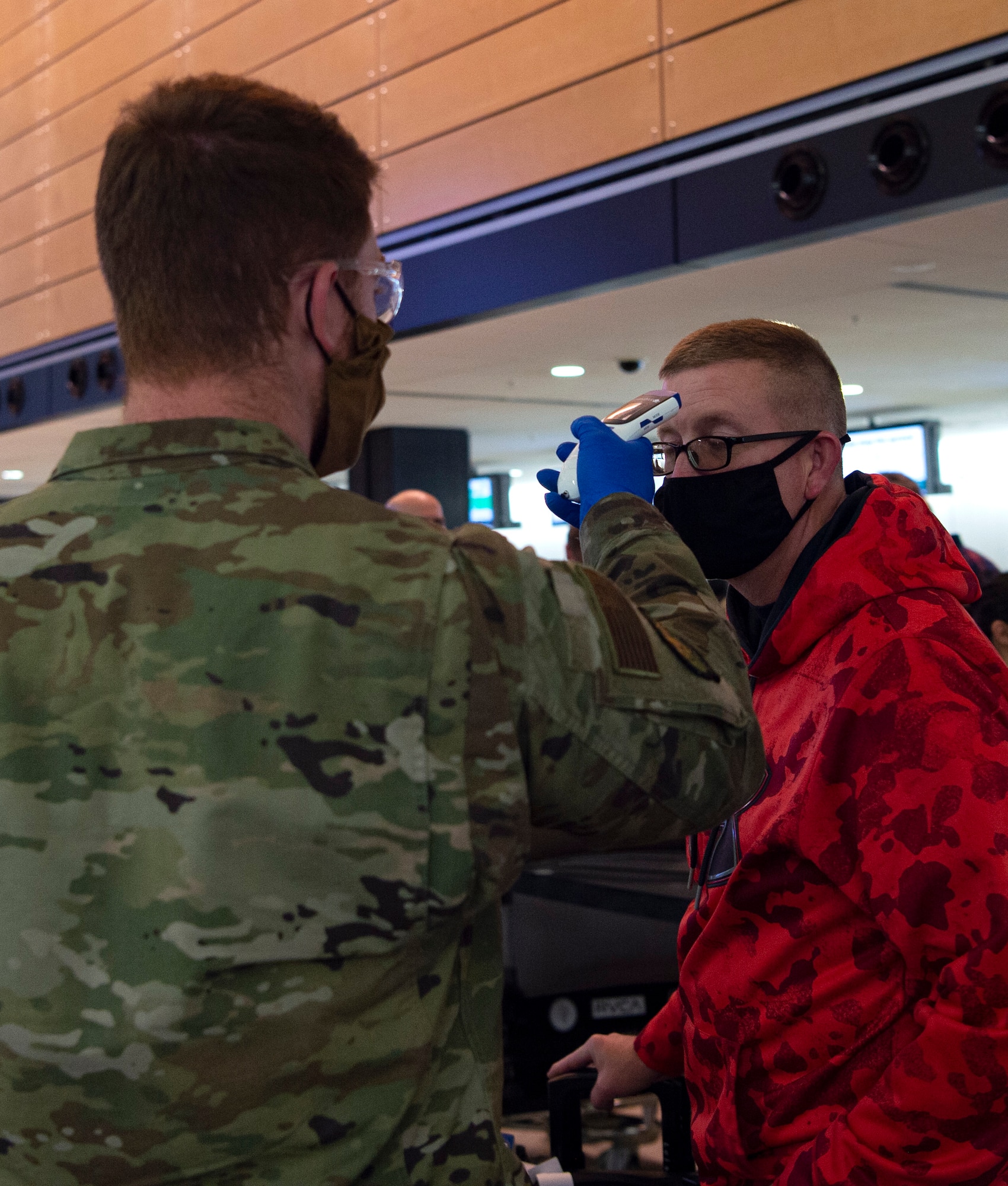 Airman 1st Class Jacob McChesney, 62nd Maintenance Squadron crew chief temporarily assigned to the 62nd Aerial Port Squadron (APS), takes the temperature of a passenger traveling to Asia at the Seattle-Tacoma International Airport in Seattle, Dec. 3, 2020. To help stop the spread of COVID-19, the 62nd APS has started random rapid COVID-19 screenings for passengers traveling through the Air Mobility Command terminal. (U.S. Air Force photo by Senior Airman Tryphena Mayhugh)