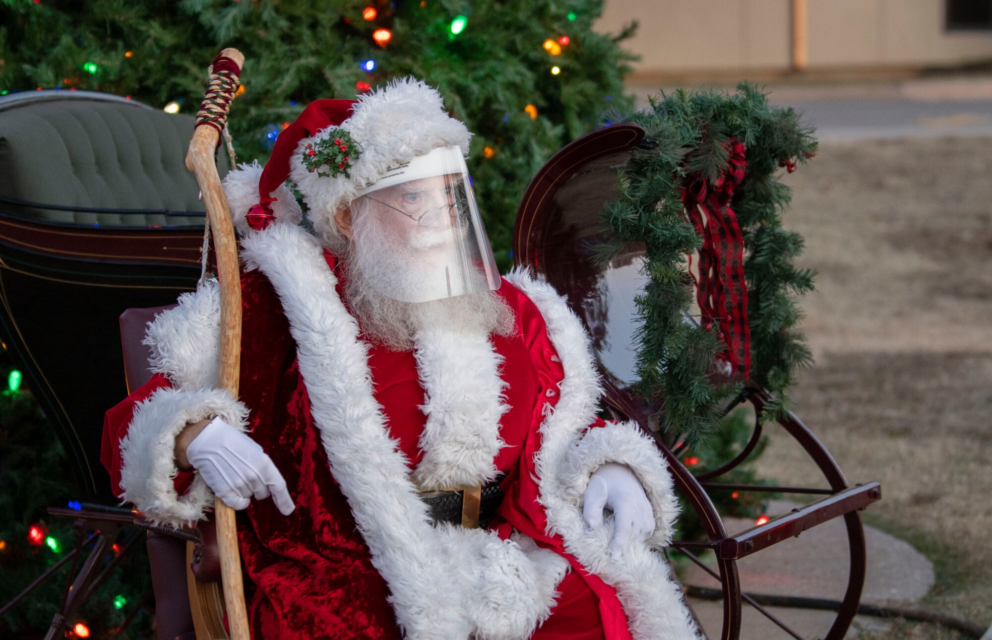 Santa Claus waits to greet family members during the annual holiday tree lighting event, Dec. 3, 2020, at Altus Air Force Base, Oklahoma. To help prevent the spread of COVID-19, Santa wore a face shield while at event. (U.S. Air Force photo by Airman 1st Class Amanda Lovelace)