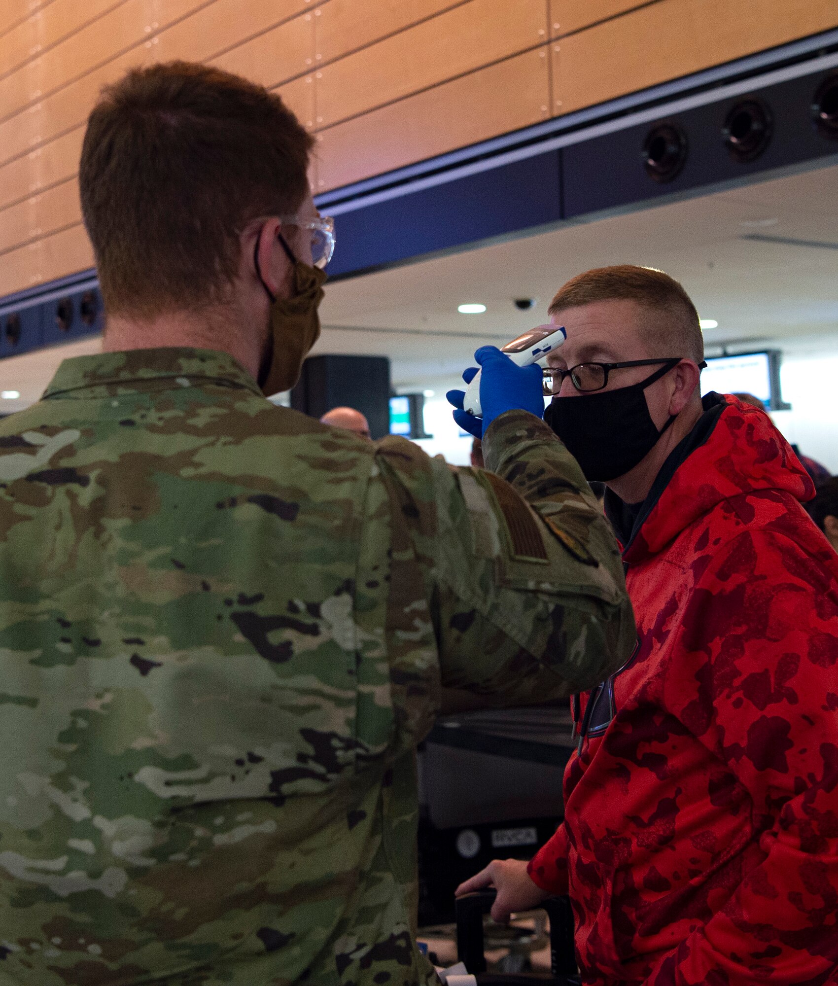 Airman 1st Class Jacob McChesney, 62nd Maintenance Squadron crew chief temporarily assigned to the 62nd Aerial Port Squadron (APS), takes the temperature of a passenger traveling to Asia at the Seattle-Tacoma International Airport in Seattle, Dec. 3, 2020. To help stop the spread of COVID-19, the 62nd APS has started random rapid COVID-19 screenings for passengers traveling through the Air Mobility Command terminal. (U.S. Air Force photo by Senior Airman Tryphena Mayhugh)