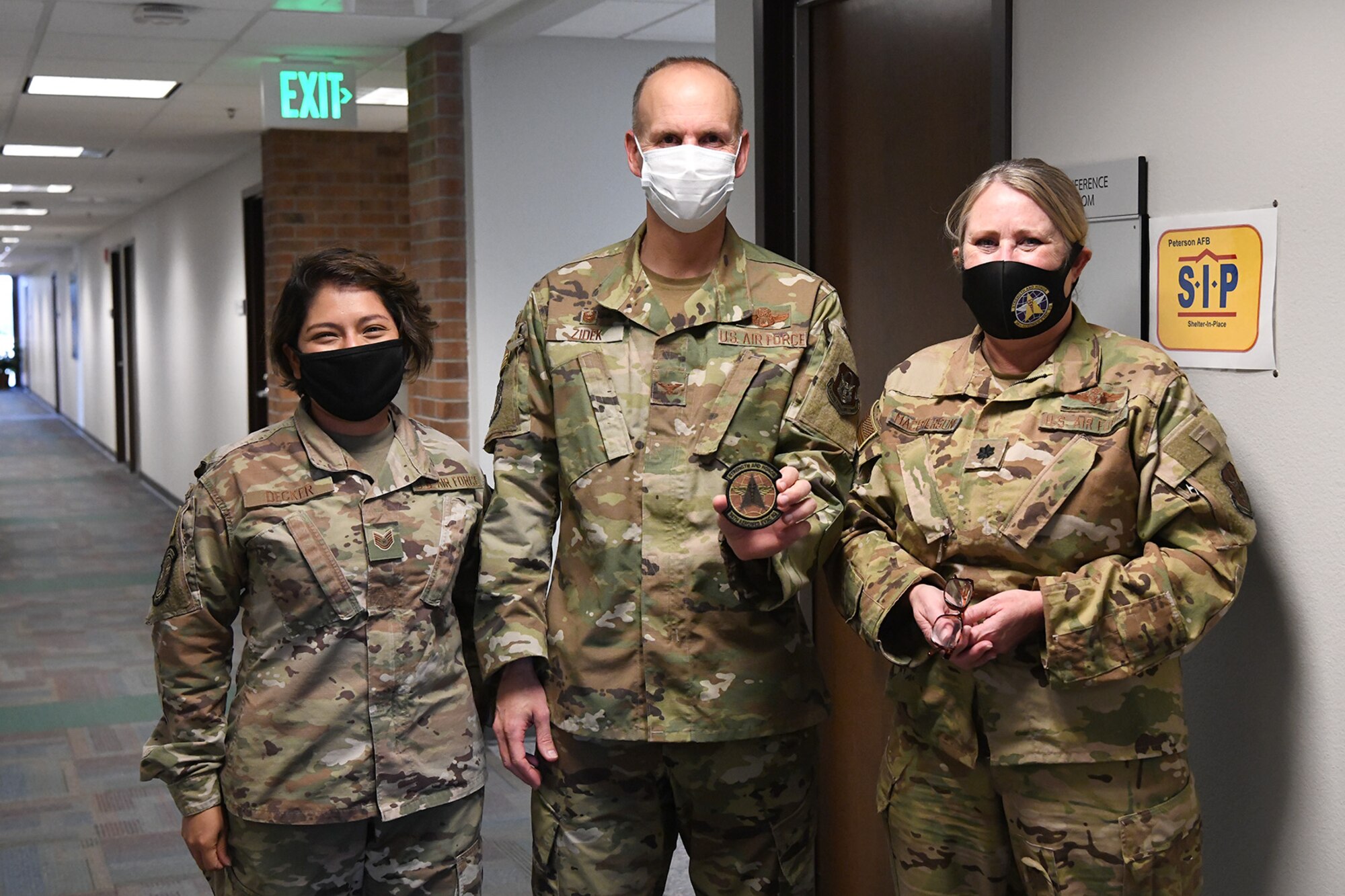 Lt. Col. Kimberly MacPherson (right), 34th Aeromedical Evacuation Squadron commander, and Tech. Sgt. Diane Decker, 34 AES medical administration Air Reserve Technician, present Col. Christopher Zidek, 302nd Airlift Wing commander, a squadron patch during his visit with the 34 AES, Dec. 6, 2020, at Peterson-Schriever Garrison, Colorado