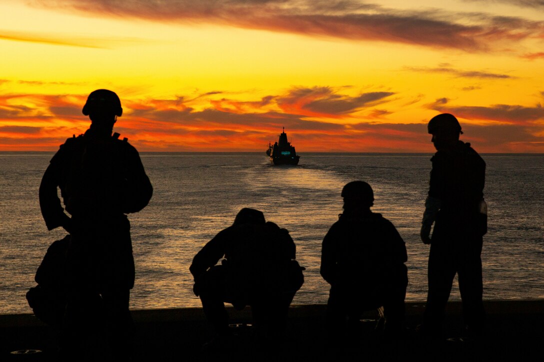 Marines and sailors post security while observing another ship at sea.