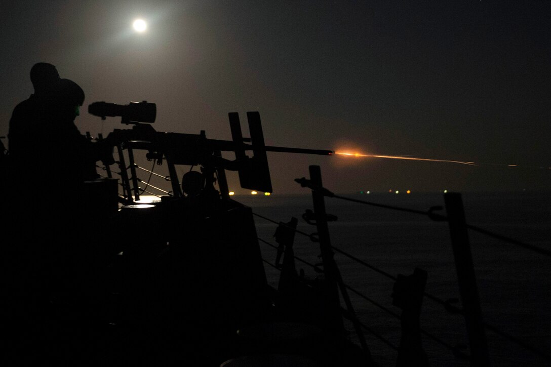 Sailors fire a weapon at night.