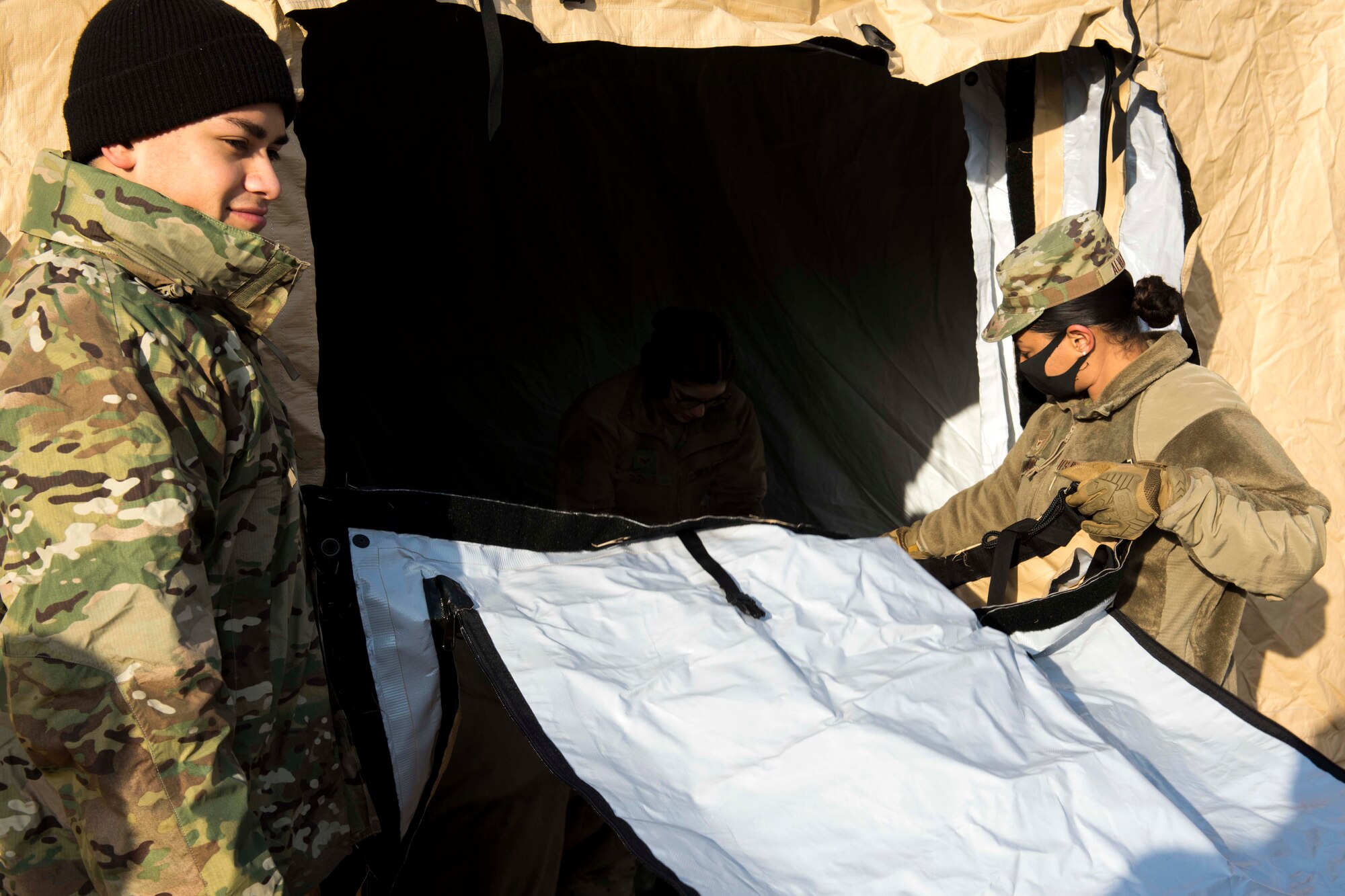 two Airmen zipping up a tent