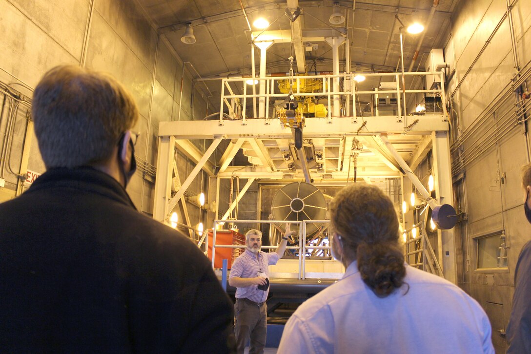 Standing in front of the F404 engine, Bernie Williamson, Aeropropulsion technology lead for the Test Systems Branch, speaks to members of the Propulsion Instrumentation Working Group in the Arnold Engineering Development Complex Sea Level 1 engine test cell at Arnold Air Force Base, Tenn., Oct. 28, 2020. The PIWG members visited Arnold to view the test facility and discuss how the test stand will be used to help mature new turbine engine instrumentation. (U.S. Air Force Photo by Deidre Moon) (This image has been altered by obscuring a badge for security purposes.)