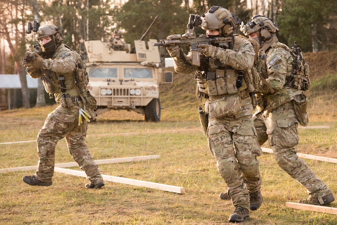 Troops with rifles drawn perform tactics in a field.