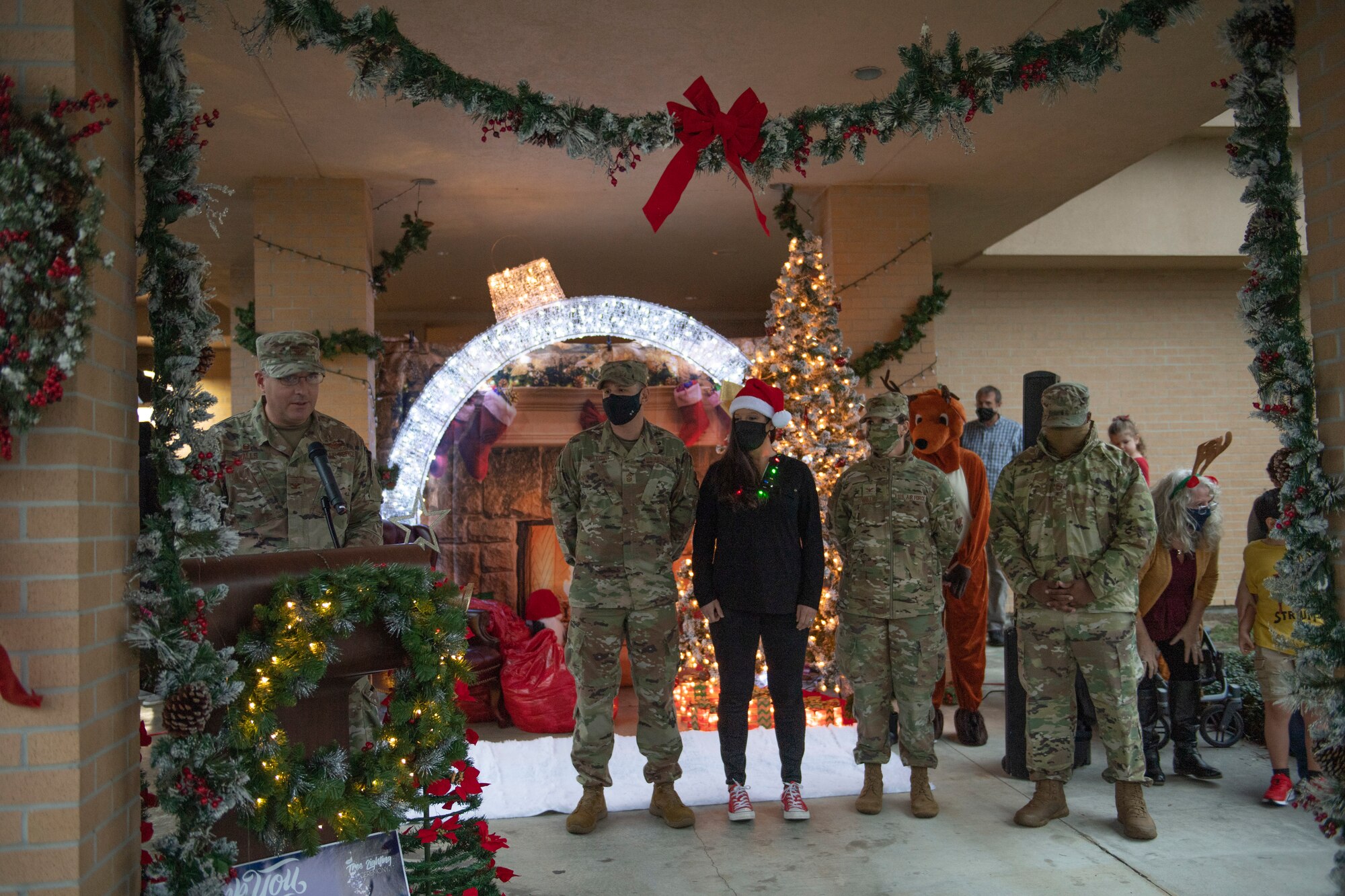 A photo of Airman standing in front of holiday decorations, while Col. Dan Walls speaks at a virtual tree-lighting ceremony.