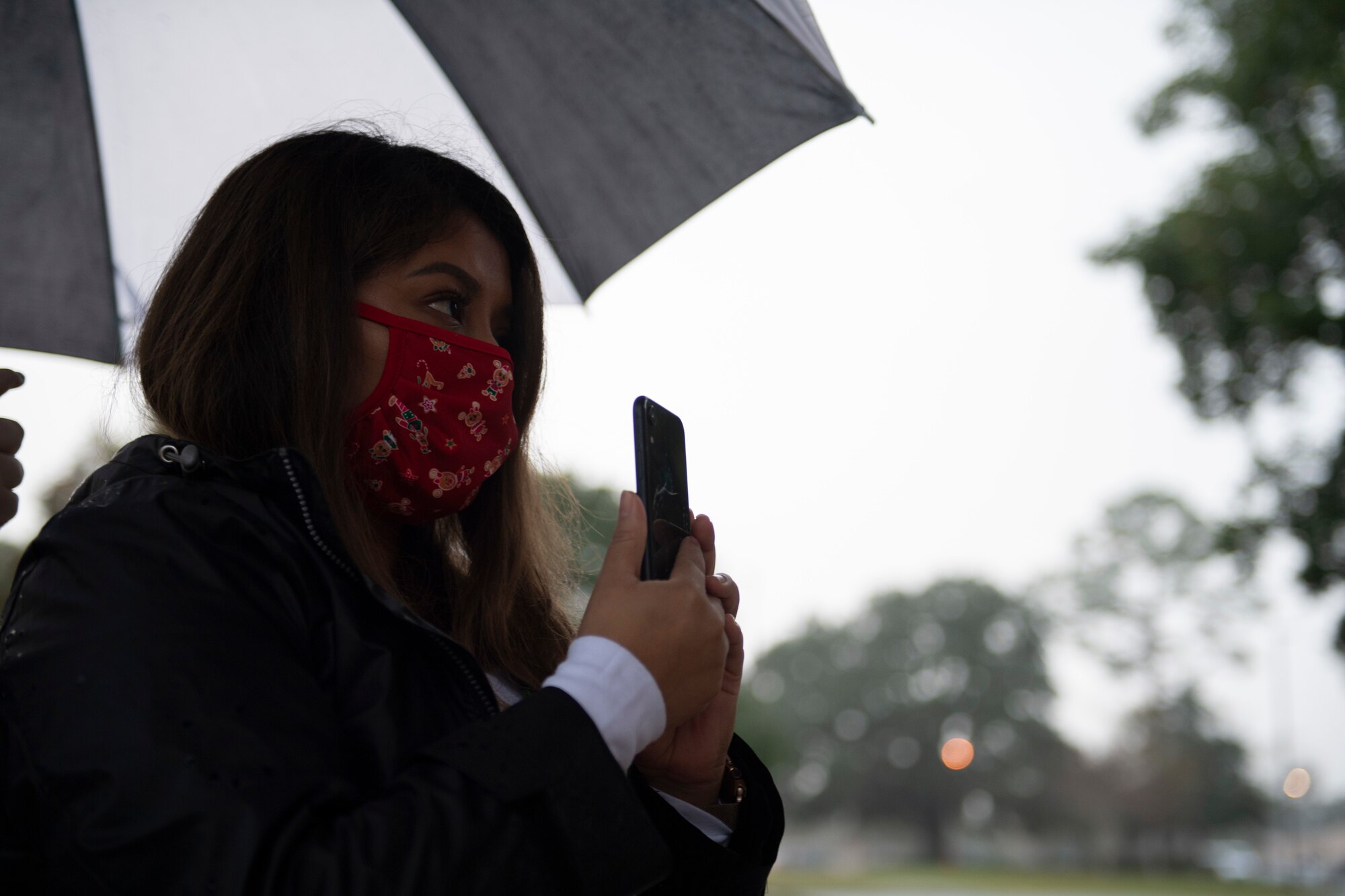 A photo of Maria Galvez holding her phone to livestream a virtual tree-lighting ceremony.