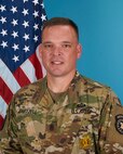 man in Army uniform standing in front of flags.