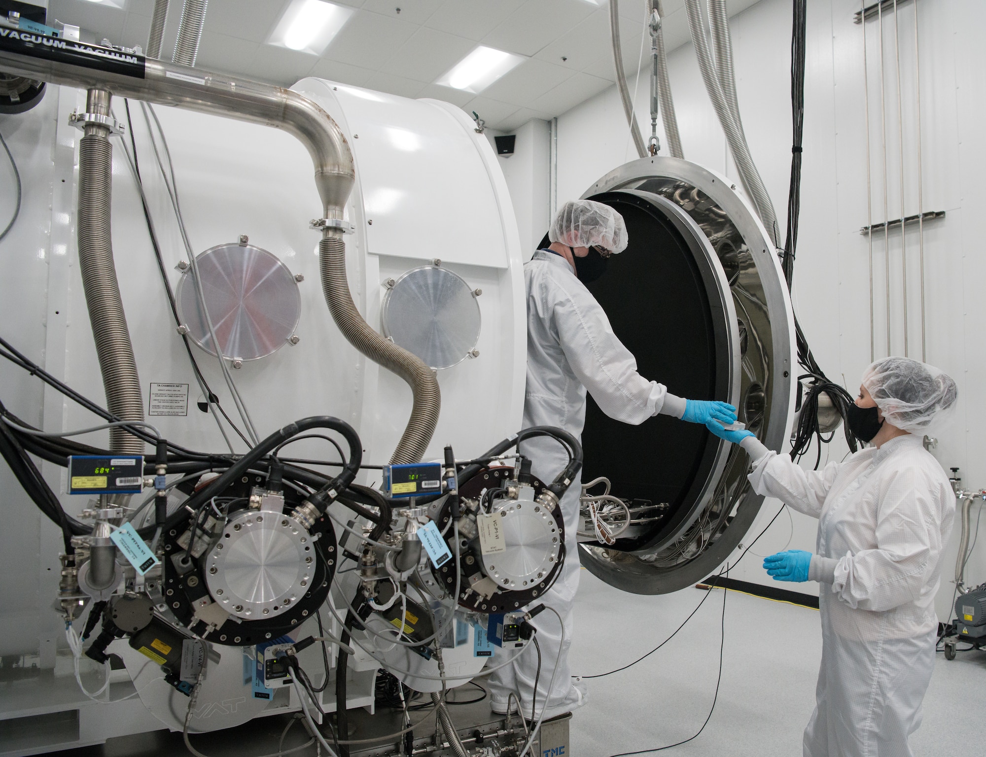 Kellye Burns, right, a space test engineer, hands a material sample to Eric D'Ambro, a test operations engineer, that will be tested in a Space Asset Resilience thermal vacuum chamber, Aug. 3, 2020, at Arnold Air Force Base, Tenn. Materials and space systems can be subjected to the natural and induced threat sources, such as protons, electrons, solar, atomic oxygen, thruster ions, material outgassing and spacecraft charging.(U.S. Air Force photo by Jill Pickett)