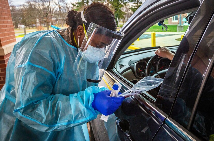 An airman wearing personal protective equipment checks the name of a staff member in their vehicle.