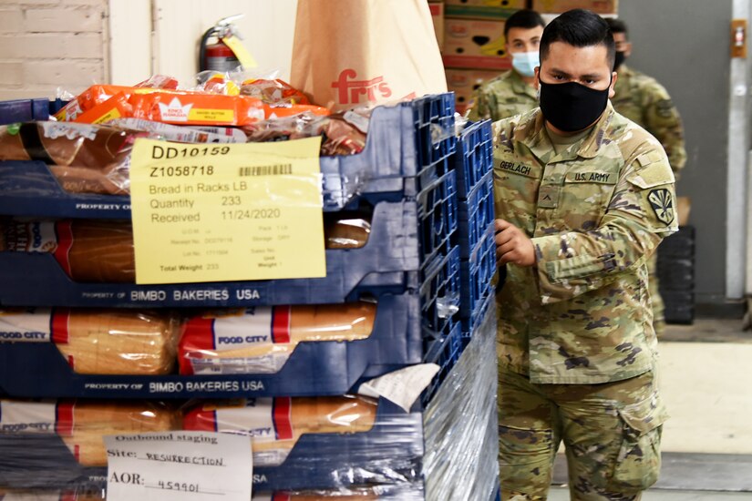 A soldier wearing a face mask pushes crates filled with food for distribution at a local food bank.