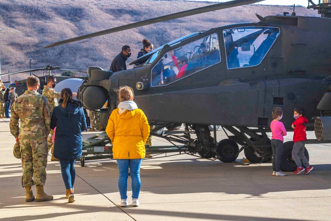 Service members, adults and children walk around parked helicopters.
