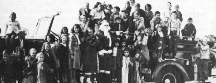 Children gather for a group photo on a firetruck at the Children's Christmas Party in 1955.