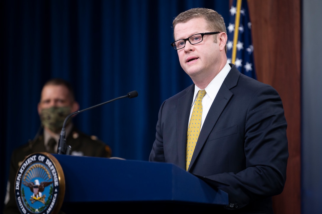 A man dressed in a suit and tie stands at a podium and speaks into a microphone.